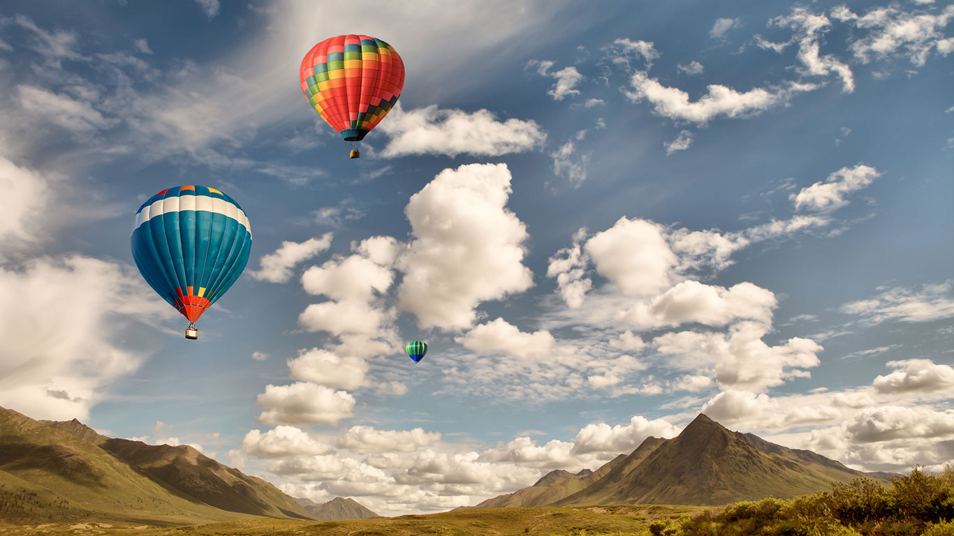 Three hot air balloons flying over mountain wilderness in Canada with puffy clouds and blue sky. (© Michele Cornelius/Alamy)(Bing Canada)