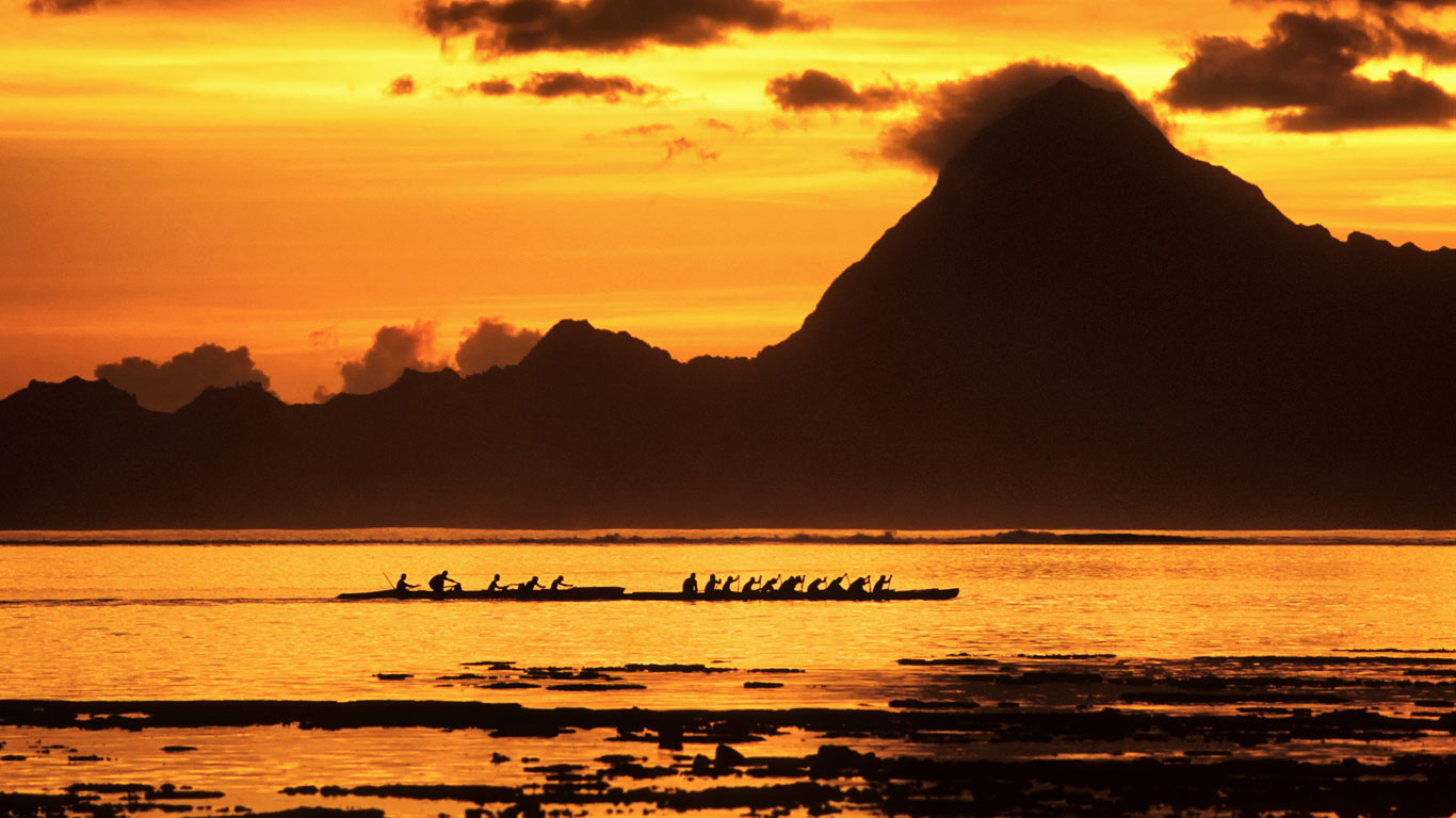 Course de pirogues polynésiennes dans le lagon au coucher du soleil, Tahiti (© Water Rights/Superstock)(Bing France)