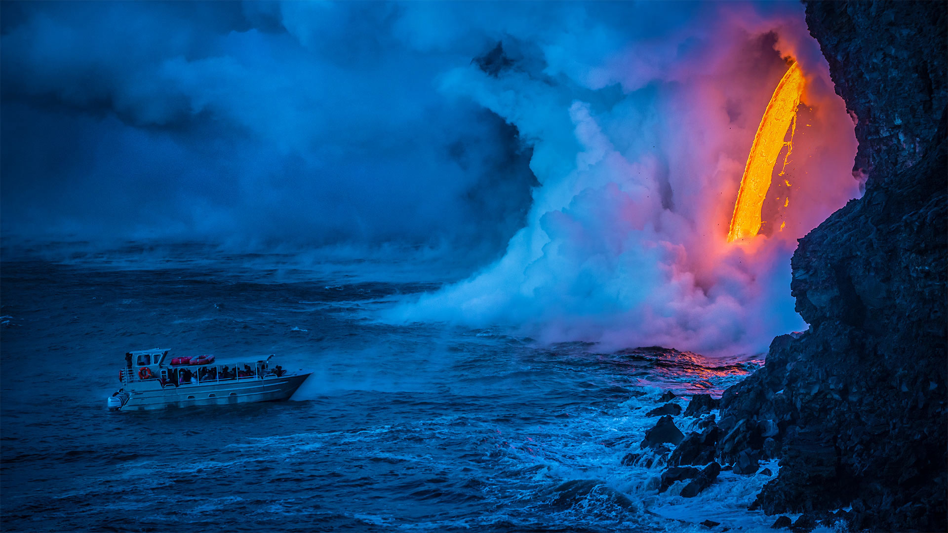 A lava flow hits water to create an explosion as a tourist boat passes, Hawaii Volcanoes National Park, USA  (© Patrick Kelley/Getty Images)(Bing United Kingdom)